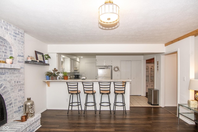 kitchen featuring dark wood-type flooring, a kitchen breakfast bar, freestanding refrigerator, a peninsula, and light countertops