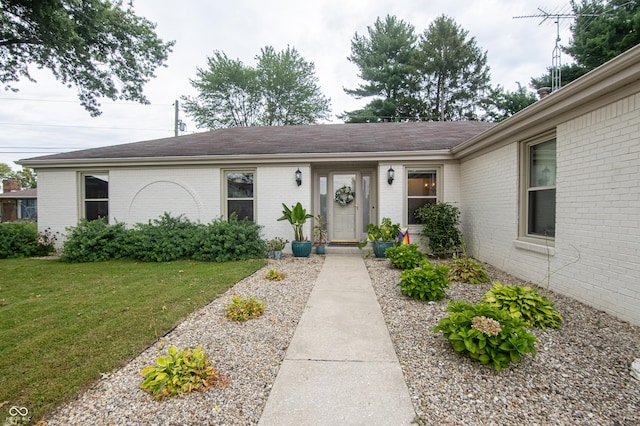 entrance to property featuring a lawn, brick siding, and roof with shingles