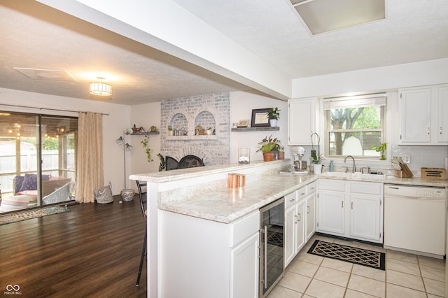 kitchen featuring beverage cooler, a peninsula, a sink, white cabinets, and dishwasher