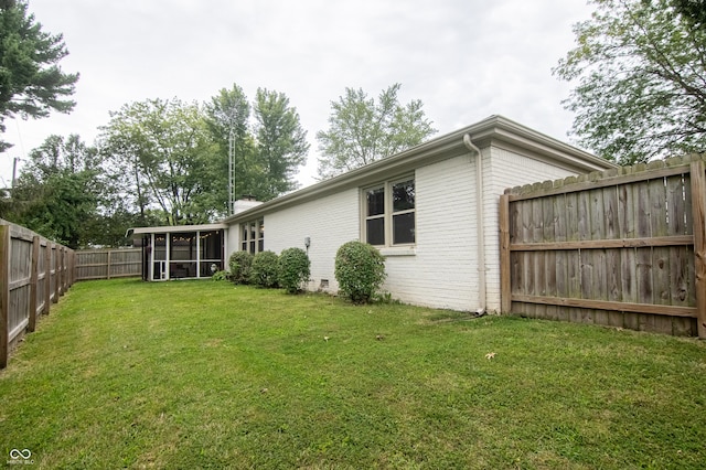 rear view of house featuring brick siding, a lawn, a fenced backyard, and a sunroom