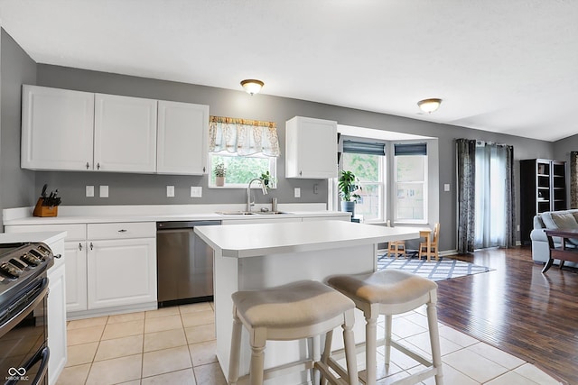 kitchen with black gas stove, a sink, white cabinets, stainless steel dishwasher, and a kitchen bar