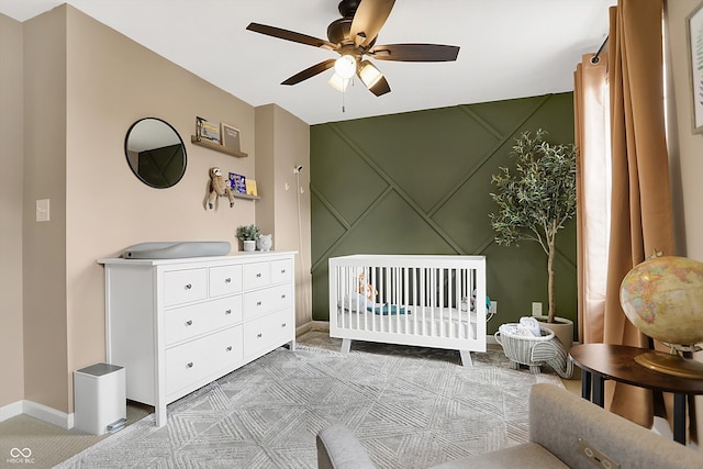 bedroom with baseboards, light carpet, a nursery area, and ceiling fan