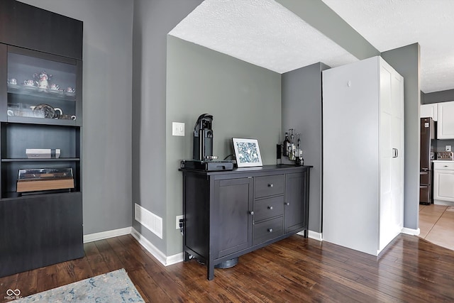 hallway with visible vents, baseboards, a textured ceiling, and dark wood-style floors