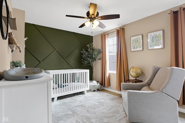 bedroom with baseboards, a crib, and a ceiling fan