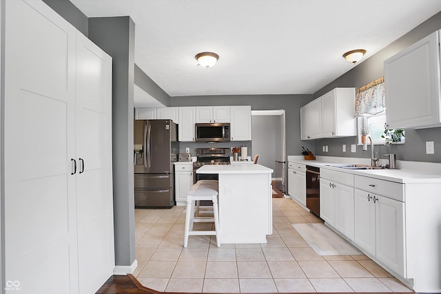 kitchen featuring a breakfast bar area, a sink, stainless steel appliances, light countertops, and white cabinetry