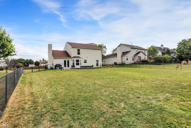 rear view of house with a yard, a fenced backyard, a chimney, and french doors