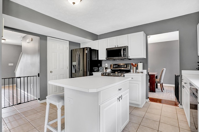 kitchen with a center island, light countertops, light tile patterned flooring, white cabinets, and stainless steel appliances