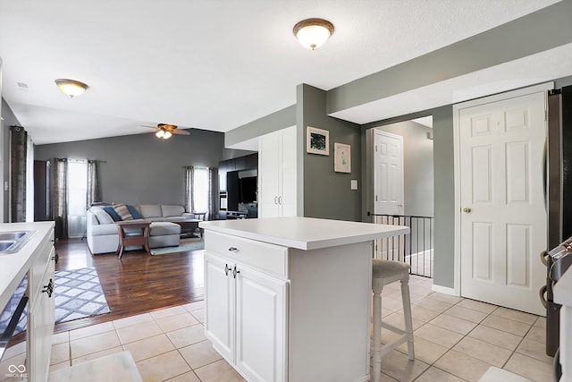 kitchen featuring vaulted ceiling, light tile patterned floors, a kitchen breakfast bar, white cabinets, and a ceiling fan