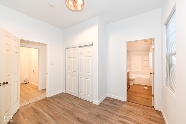 unfurnished bedroom with a closet, light wood-style flooring, ensuite bathroom, and baseboards