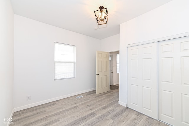 unfurnished bedroom with light wood finished floors, a notable chandelier, a closet, and baseboards