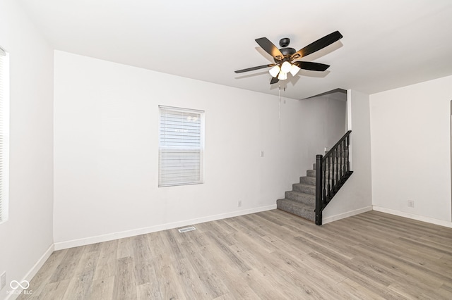 unfurnished room featuring light wood finished floors, stairway, baseboards, and a ceiling fan