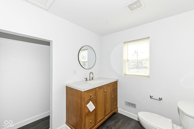 half bathroom featuring vanity, toilet, wood finished floors, and visible vents