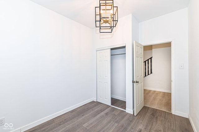 unfurnished bedroom with dark wood finished floors, a chandelier, a closet, and baseboards