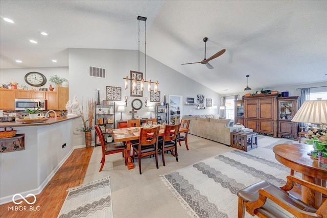 dining area with visible vents, ceiling fan, lofted ceiling, light wood-style floors, and a textured ceiling