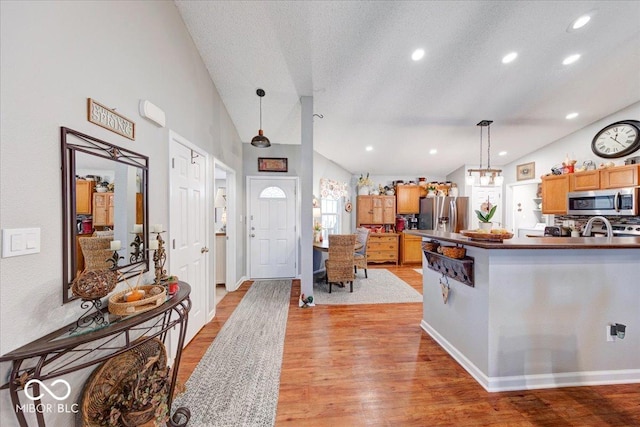 kitchen with lofted ceiling, light wood-style flooring, hanging light fixtures, appliances with stainless steel finishes, and dark countertops