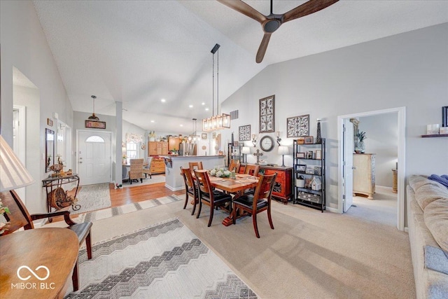 dining space with visible vents, high vaulted ceiling, ceiling fan with notable chandelier, baseboards, and light colored carpet