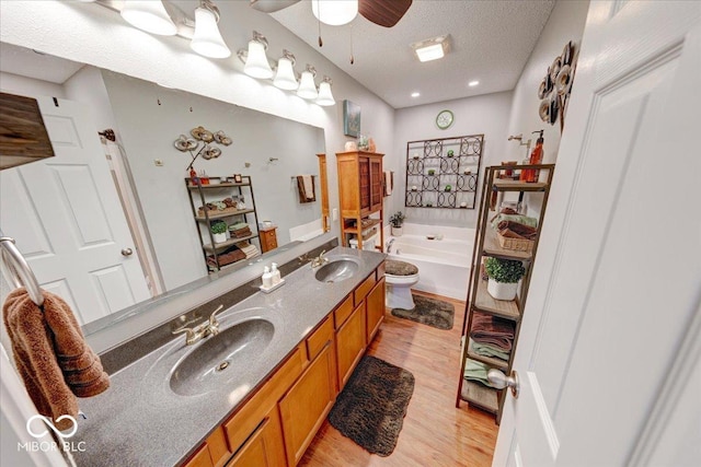 bathroom with ceiling fan, wood finished floors, a garden tub, and a sink