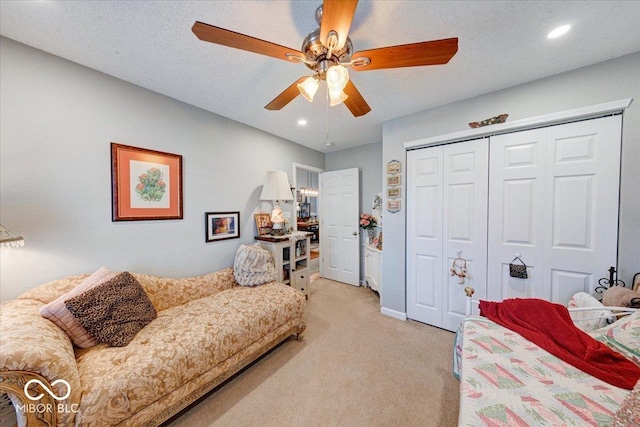 bedroom featuring ceiling fan, light colored carpet, a closet, and a textured ceiling