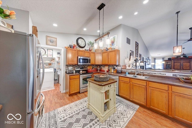 kitchen with washing machine and clothes dryer, lofted ceiling, light wood-style flooring, appliances with stainless steel finishes, and a sink