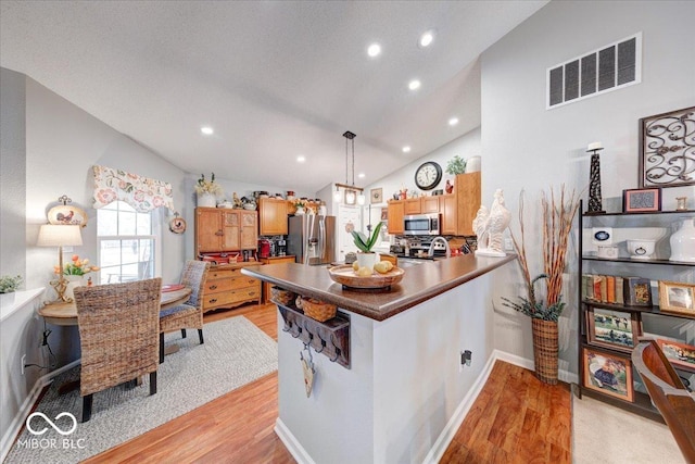 kitchen with visible vents, a peninsula, light wood-style flooring, appliances with stainless steel finishes, and dark countertops