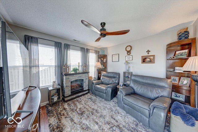 living room featuring visible vents, a fireplace, a textured ceiling, and a ceiling fan