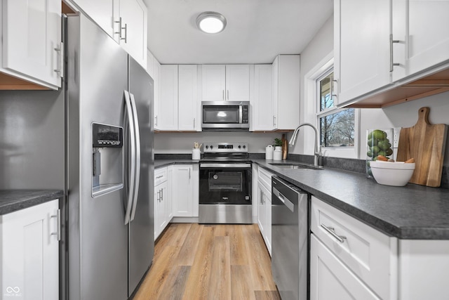 kitchen with a sink, dark countertops, stainless steel appliances, light wood-style floors, and white cabinets