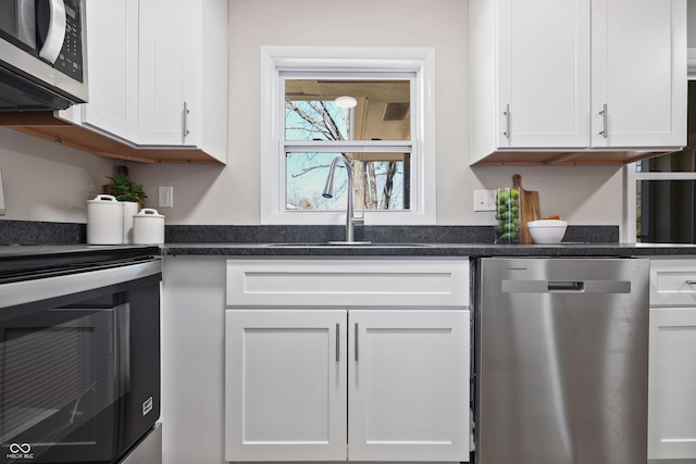 kitchen with a sink, dark stone countertops, white cabinets, and stainless steel appliances