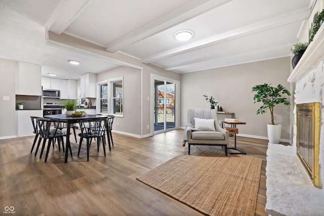 dining room featuring beam ceiling, a glass covered fireplace, light wood-style flooring, and baseboards