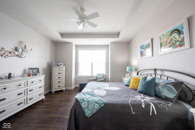 bedroom featuring a tray ceiling, baseboards, dark wood-type flooring, and ceiling fan