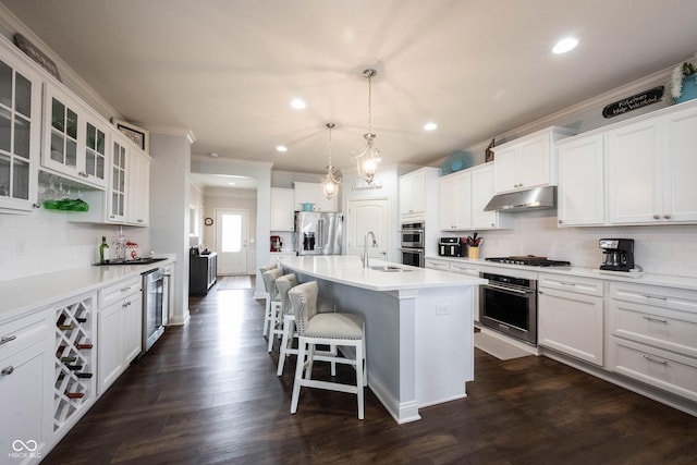 kitchen featuring under cabinet range hood, a sink, backsplash, appliances with stainless steel finishes, and a breakfast bar area