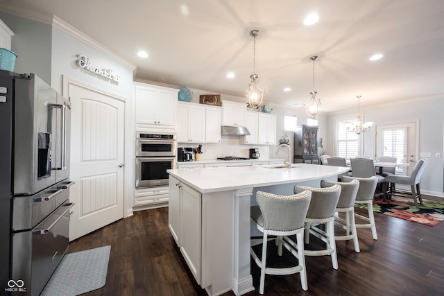 kitchen featuring under cabinet range hood, light countertops, ornamental molding, appliances with stainless steel finishes, and dark wood-style flooring