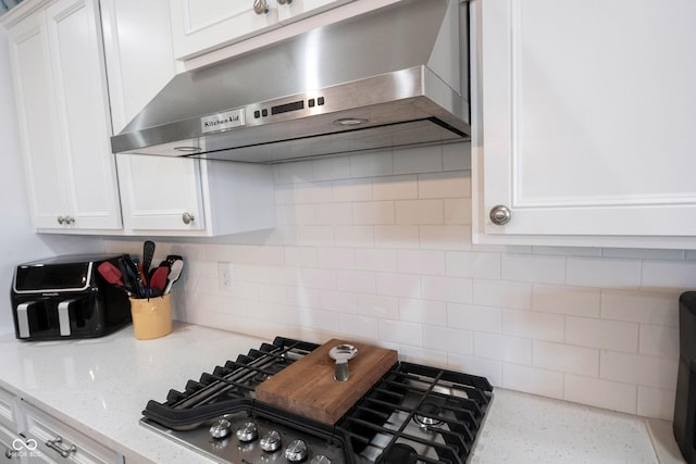 kitchen with under cabinet range hood, stainless steel gas cooktop, light stone counters, decorative backsplash, and white cabinets