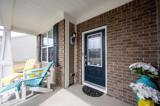 doorway to property featuring brick siding and covered porch