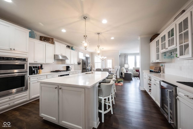 kitchen with under cabinet range hood, wine cooler, ornamental molding, stainless steel appliances, and a sink