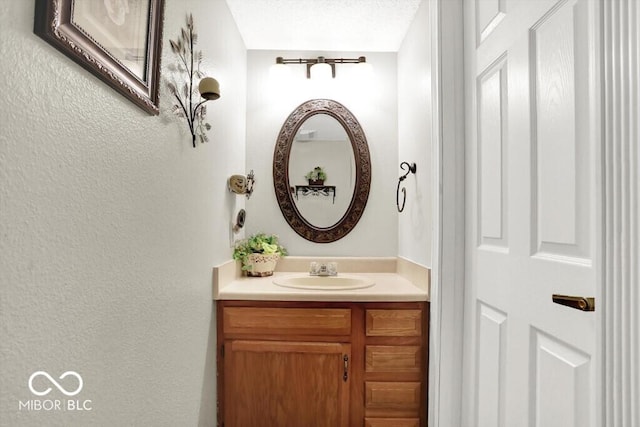 bathroom with a textured ceiling, vanity, and a textured wall