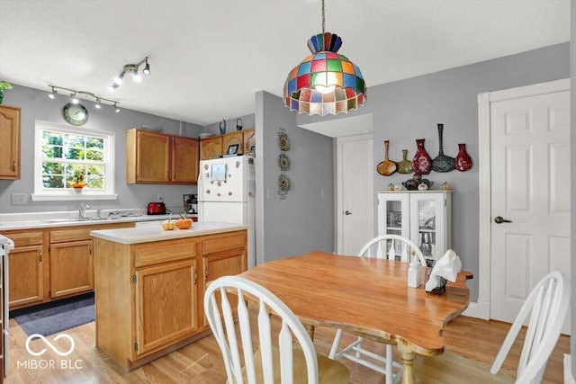 kitchen with light wood-type flooring, a sink, a center island, freestanding refrigerator, and light countertops