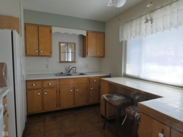 kitchen with a sink, ceiling fan, brown cabinetry, and freestanding refrigerator