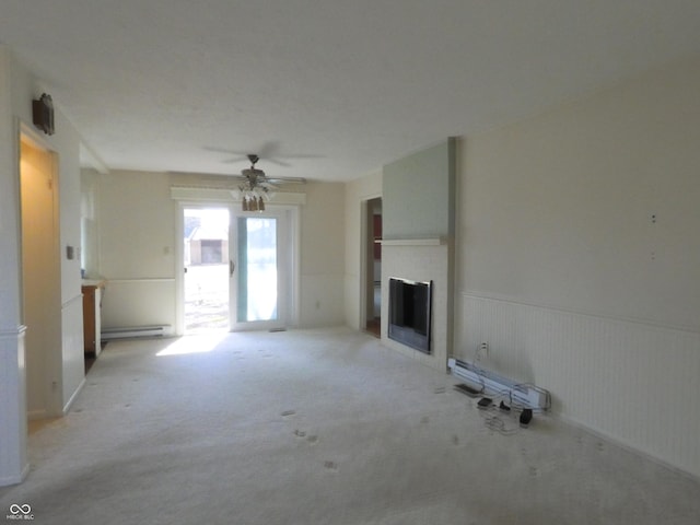 unfurnished living room featuring a wainscoted wall, light carpet, a ceiling fan, a baseboard heating unit, and a fireplace