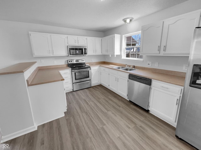 kitchen with a sink, stainless steel appliances, white cabinets, and light wood finished floors