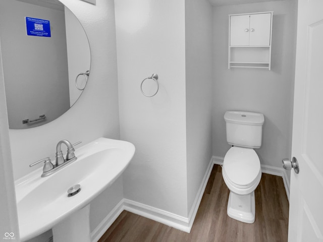 bathroom with toilet, wood finished floors, baseboards, and a sink