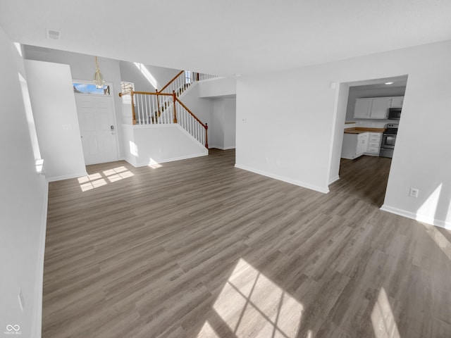 unfurnished living room with stairs, visible vents, wood finished floors, and baseboards