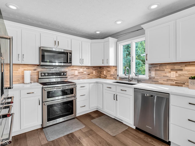 kitchen with a sink, dark wood-style floors, white cabinetry, stainless steel appliances, and light countertops