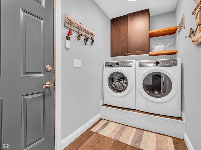 washroom featuring wood finished floors, washing machine and dryer, cabinet space, and baseboards