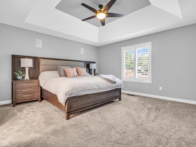 bedroom with a tray ceiling, baseboards, visible vents, and light carpet