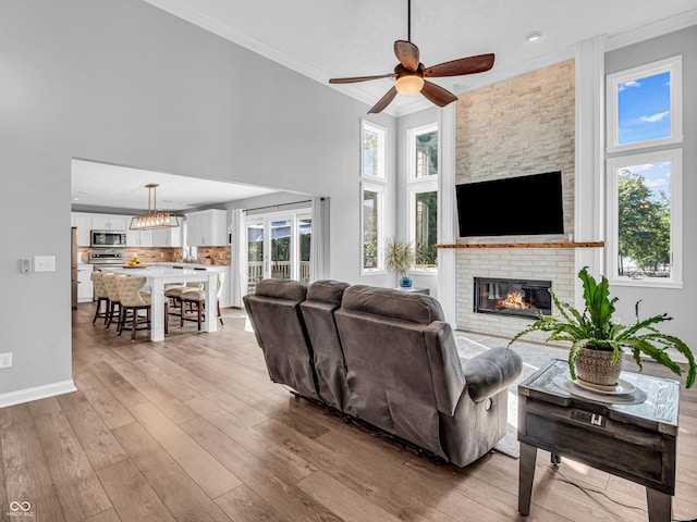 living area featuring light wood finished floors, crown molding, a wealth of natural light, ceiling fan with notable chandelier, and a fireplace