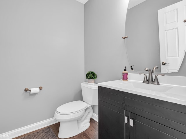 half bath with baseboards, toilet, wood finished floors, and vanity