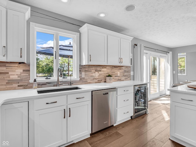 kitchen with wine cooler, stainless steel dishwasher, wood finished floors, white cabinets, and a sink