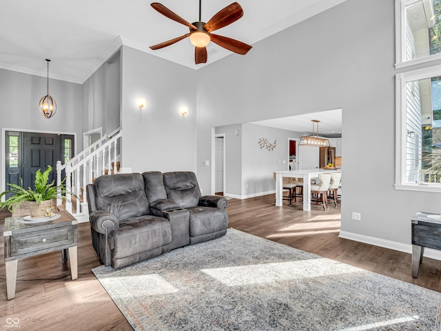 living room featuring stairway, a high ceiling, wood finished floors, and ceiling fan with notable chandelier