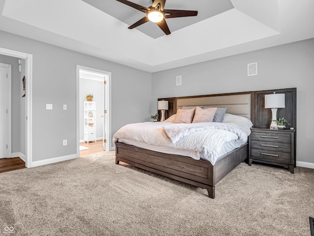 bedroom featuring a raised ceiling, ensuite bathroom, carpet floors, baseboards, and ceiling fan