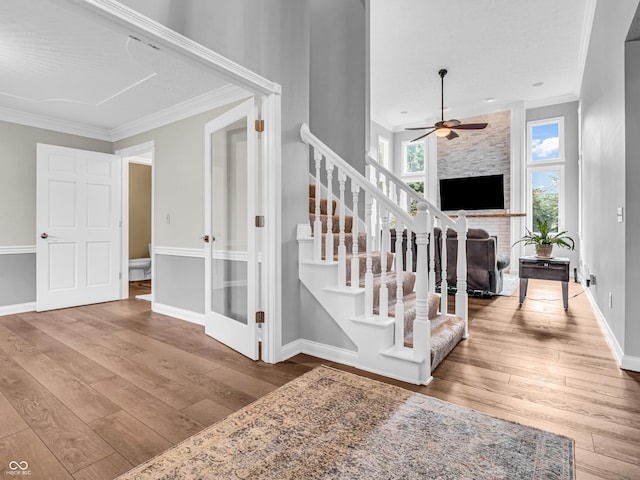 stairs with hardwood / wood-style flooring, crown molding, baseboards, a brick fireplace, and ceiling fan